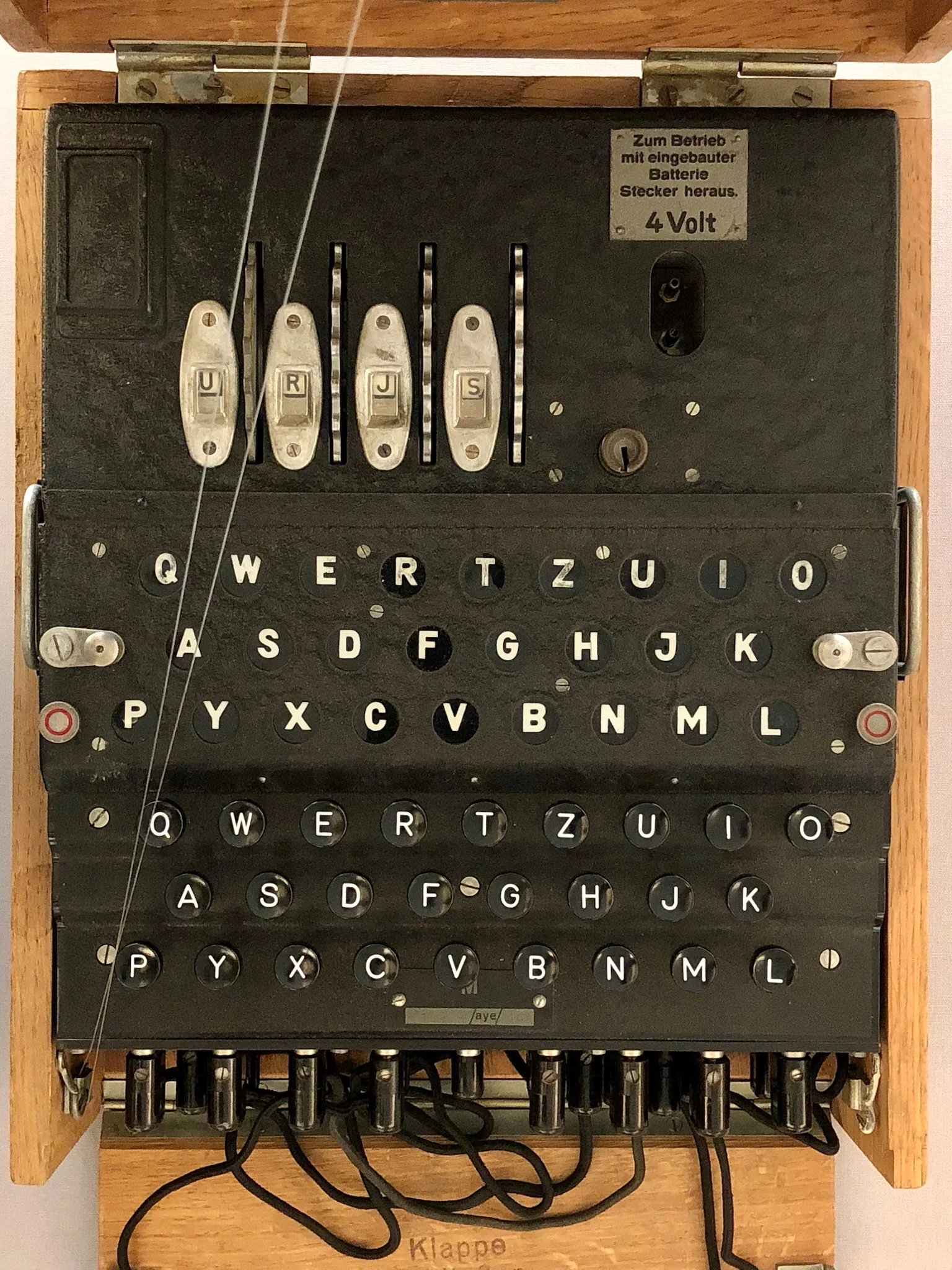 An Enigma M4 cipher machine in its wooden case: lamp board, keyboard, plugboard at the front, four rotors visible above.